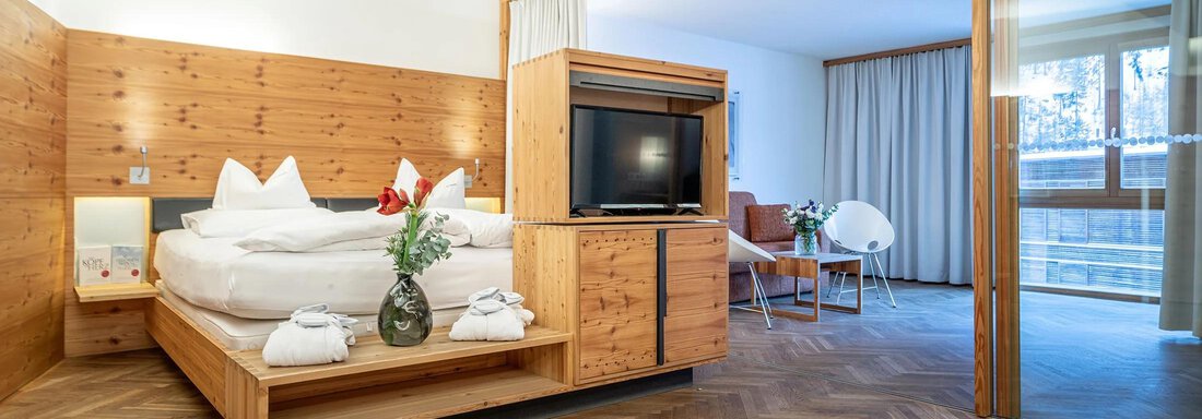 Hotel Liebe Sonne Wellness Suite Soelderkogl | © Hotel Liebe Sonne (CC C) A modern hotel room with warm wood details and a large bed. The room features a television and a cozy seating area. - Hotel Liebe Sonne - Sölden