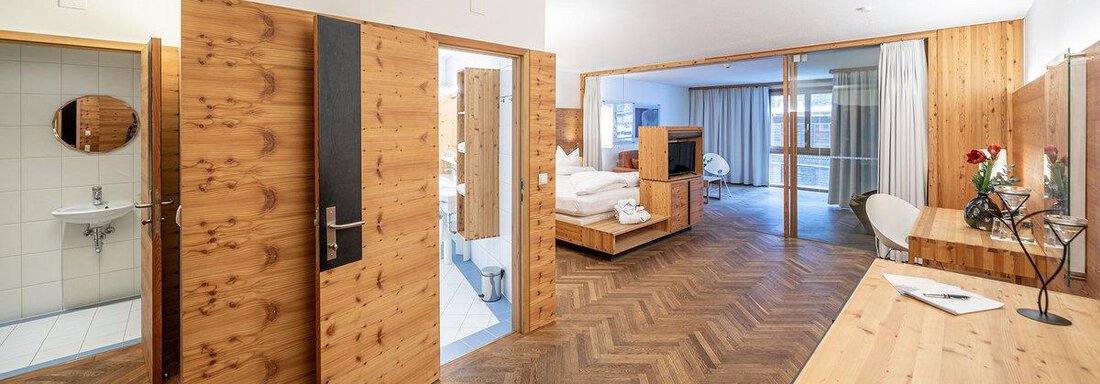 A modern room with wood paneling and an elegant parquet floor. There are separate areas for the bed and bathroom, as well as a cozy seating area. - Hotel Liebe Sonne - Sölden