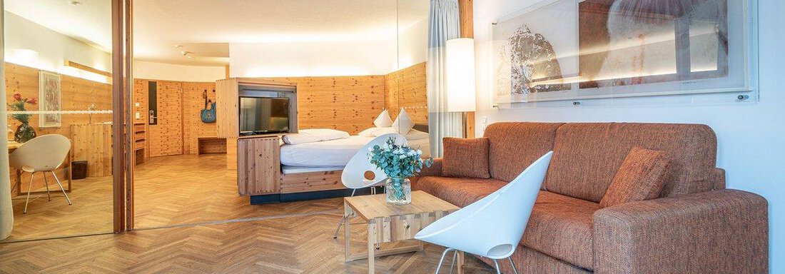 A modern room with a cozy sofa, a table, and a television. In the background, a bed and decorative elements are visible. - Hotel Liebe Sonne - Sölden