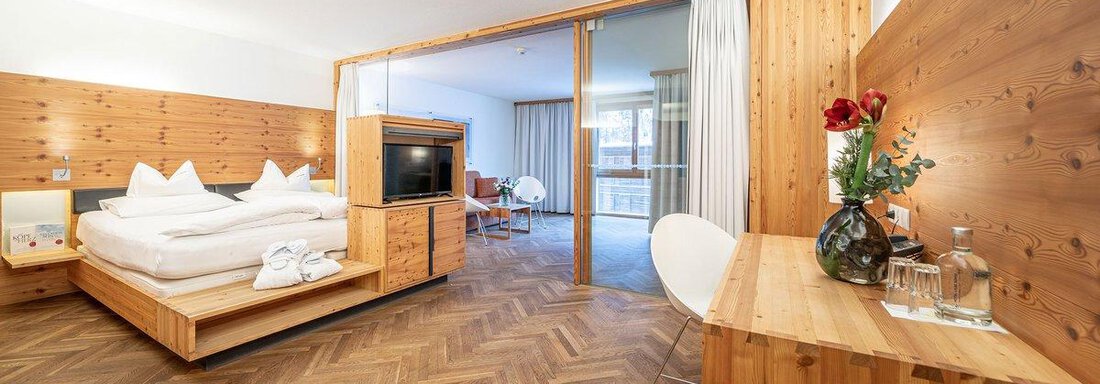 A modern room with wooden walls and a large window. There is a double bed, a television, and a cozy seating area. - Hotel Liebe Sonne - Sölden