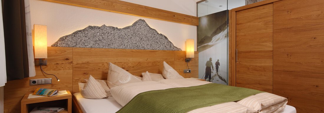 A cozy bedroom with a wooden bed and soft colors. The walls are tastefully designed, and a modern bathroom is visible. - Hotel Sportpension Carinthia - Sölden