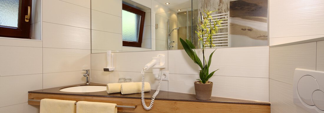 A modern bathroom with a wooden shelf and washbasin. The plants and towels give the space an inviting atmosphere. - Hotel Sportpension Carinthia - Sölden
