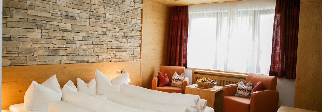 A cozy bedroom with a large bed and pillows. The walls are made of wood and the windows let in a lot of light. - Hotel Sportpension Carinthia - Sölden