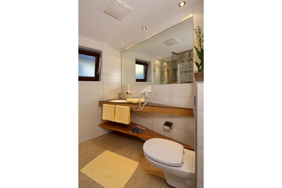 A modern bathroom with a bright tiled floor and a large mirror. Wooden shelves with towels and a plant complete the design. - Hotel Sportpension Carinthia - Sölden