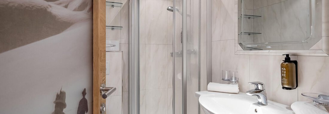 A modern bathroom with a glass shower cabin and a sink. There are also towels and a mirror surface. - Hotel Sportpension Carinthia - Sölden