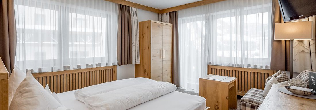A modern bedroom with wooden furniture and large windows. The pleasant atmosphere is enhanced by plenty of daylight and a cozy decor. - Hotel Sportpension Carinthia - Sölden