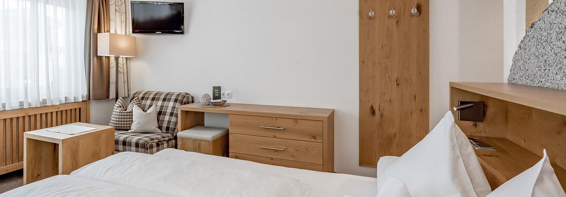 A modern bedroom with two beds, a wooden wardrobe, and a television. Large windows provide plenty of daylight and a cozy atmosphere. - Hotel Sportpension Carinthia - Sölden