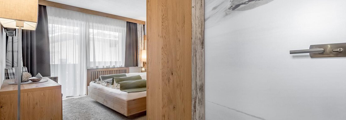 A modern room with wooden furniture and a cozy bed. The room has large windows that let in plenty of light. - Hotel Sportpension Carinthia - Sölden