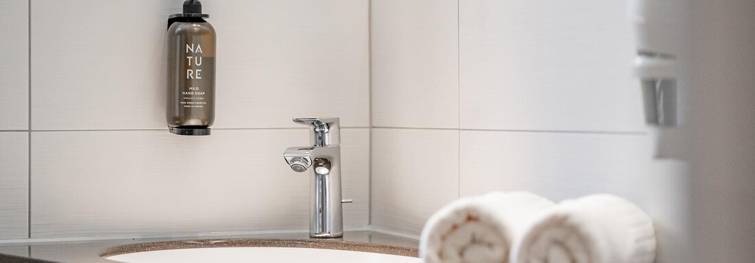 A modern bathroom with a smooth surface and a round sink. Next to the sink are two freshly rolled towels. - Hotel Sportpension Carinthia - Sölden