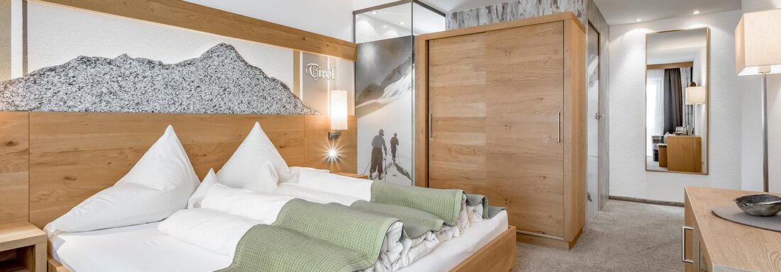 carin_zimmer_katB_1 A modern hotel room with wooden decor and a large bed. The walls are designed with decorative elements and mirrors. - Hotel Sportpension Carinthia - Sölden