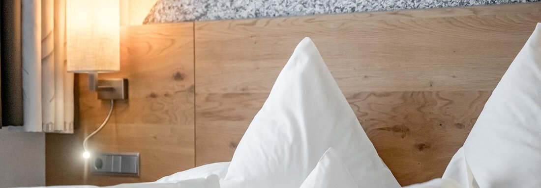 A comfortable bed with white pillows and a green blanket in a modern room. On the wall, there is a stylish lamp and a decorative stone surface. - Hotel Sportpension Carinthia - Sölden