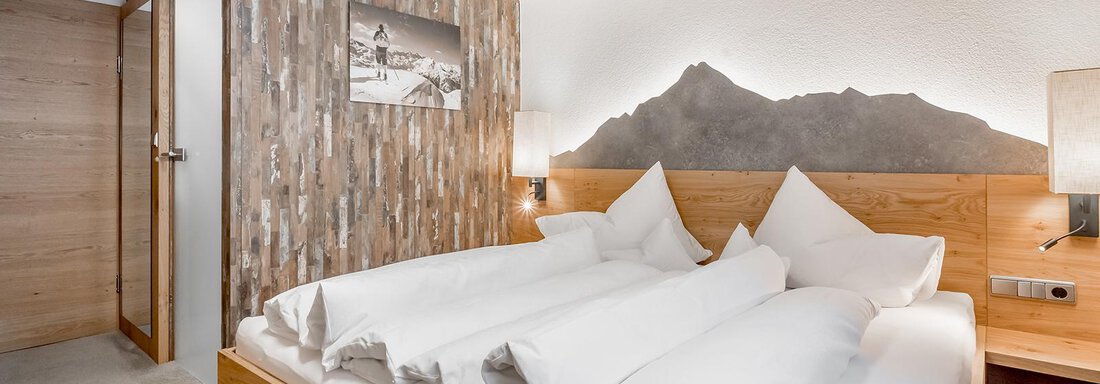 carin_zimmer_katC_1 A cozy bedroom with a large double bed and pillows. The wood paneling on the walls creates a warm, inviting atmosphere. - Hotel Sportpension Carinthia - Sölden
