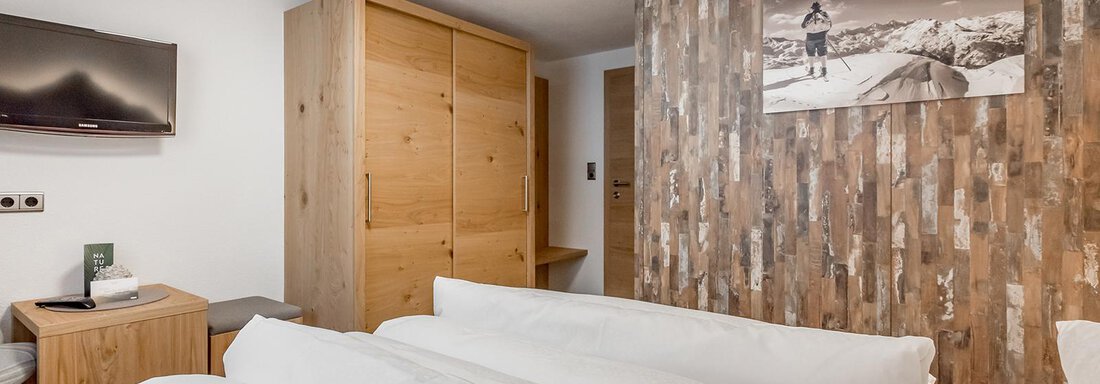 A modern room with a large bed and wooden decor. The furnishings include a television and a wooden wardrobe. - Hotel Sportpension Carinthia - Sölden