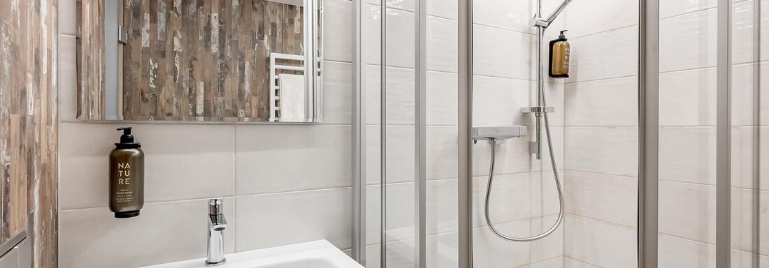 A modern bathroom with a shower and a sink. The walls are tiled in light colors and have wooden accents. - Hotel Sportpension Carinthia - Sölden