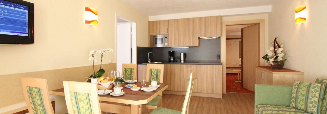 A modern living room with a cozy seating area and a dining table. The kitchen is open and well-equipped, with a bright and inviting atmosphere. - Hotelappart Peter - Sölden