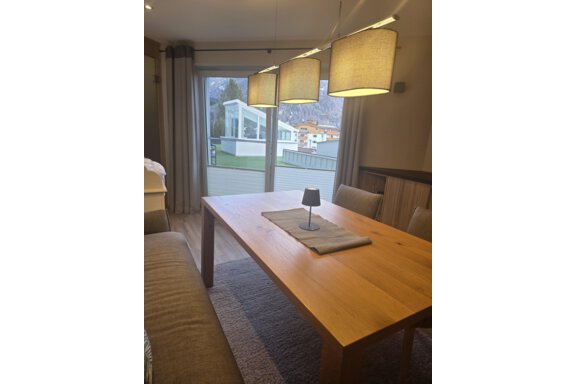 A modern dining area with a wooden table and cozy chairs. Large windows offer a view of the outdoor landscape. - Hotelappart Peter - Sölden