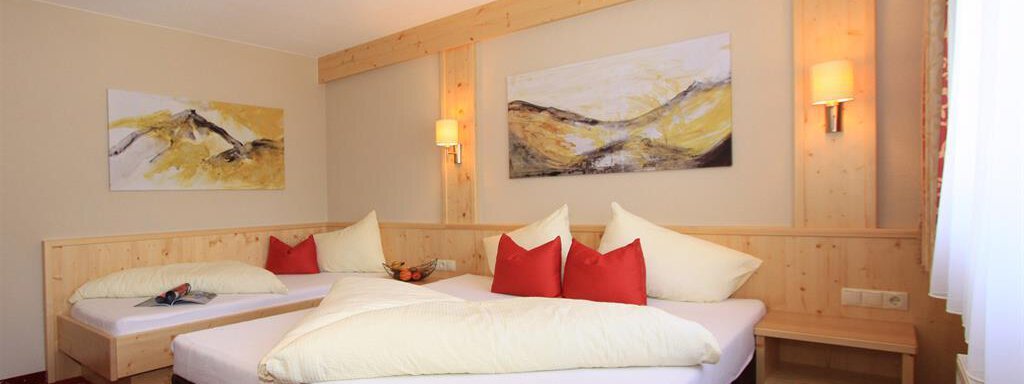 A cozy bedroom with two beds and red pillows. Modern artworks hang on the walls, and the room has warm lighting. - Hotelappart Peter - Sölden