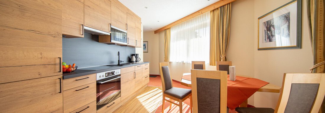 A modern kitchen with wooden cabinets and a dining table. Bright and inviting with plenty of natural light. - Hotelappart Peter - Sölden