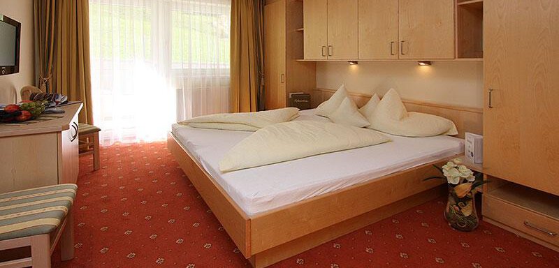 A cozy bedroom with a large double bed and modern furniture. The room has light curtains and a small seating area. - Hotelappart Peter - Sölden