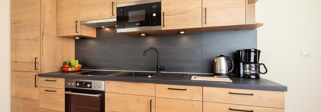 A modern kitchen with wooden fronts and a black worktop. It is well-equipped with a stove, a microwave, and a kettle. - Hotelappart Peter - Sölden