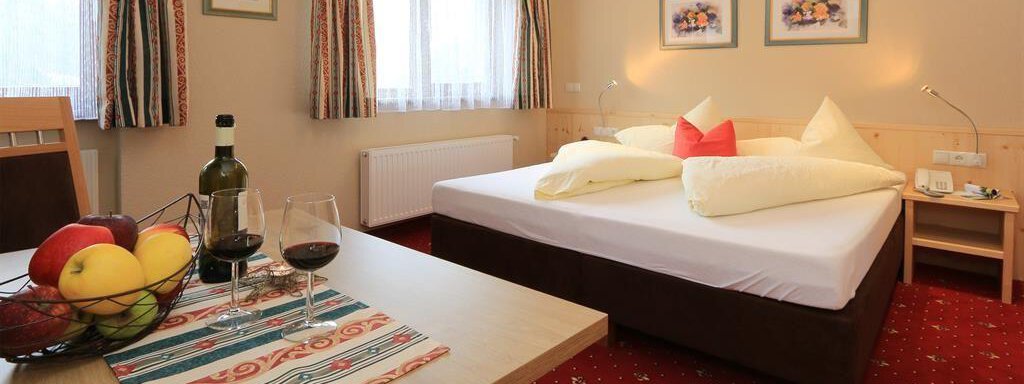 A cozy room with a double bed and colorful cushions. Fresh fruit, wine, and glasses are on the table. - Hotelappart Peter - Sölden