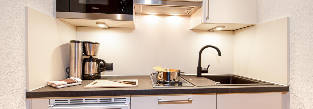 Küche 6a A modern kitchen nook with a cooktop, a faucet, and a microwave oven. There is also a coffee machine and kitchen utensils on the countertop. - Hotelappart Peter - Sölden