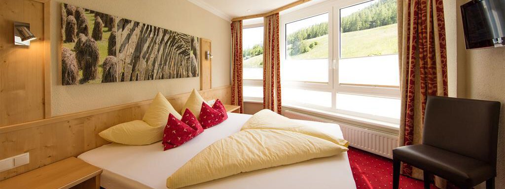 A cozy bedroom with a large double bed and colorful cushions. The large windows offer a view of the green landscape outside. - Hotelappart Peter - Sölden