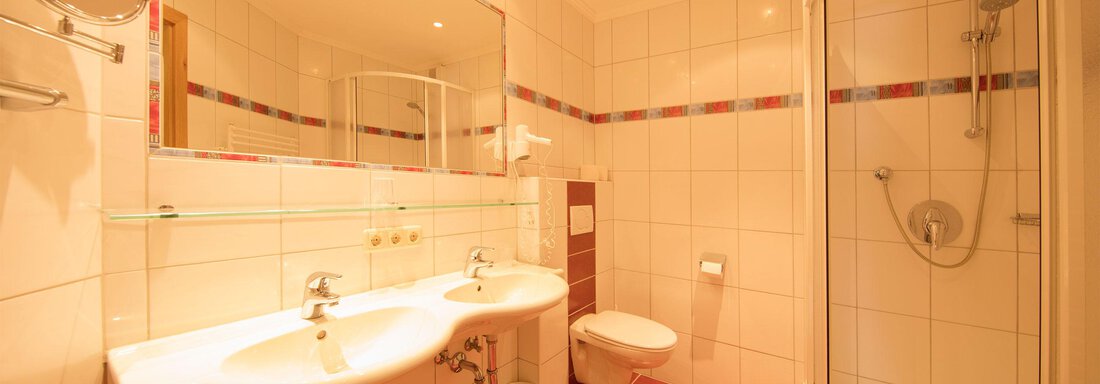A modern bathroom with two sinks and a shower. Bright tiles and good lighting create an inviting atmosphere. - Hotelappart Peter - Sölden