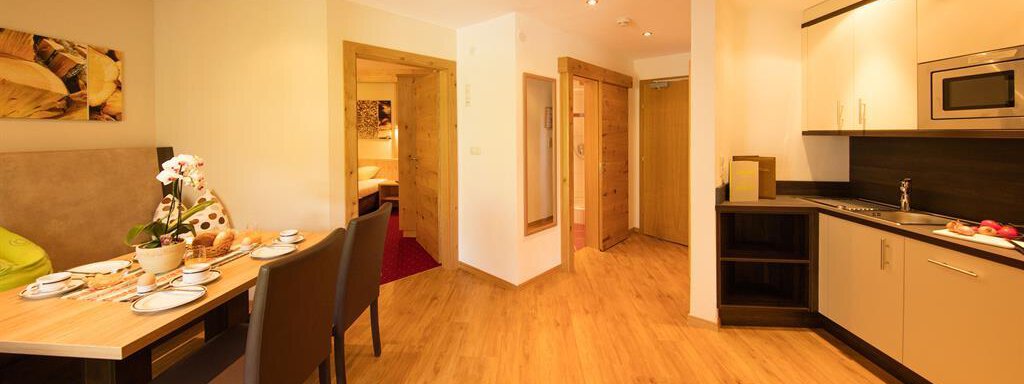 A modern apartment with an open kitchen and a dining area. The space features wooden flooring and light walls, creating an inviting atmosphere. - Hotelappart Peter - Sölden