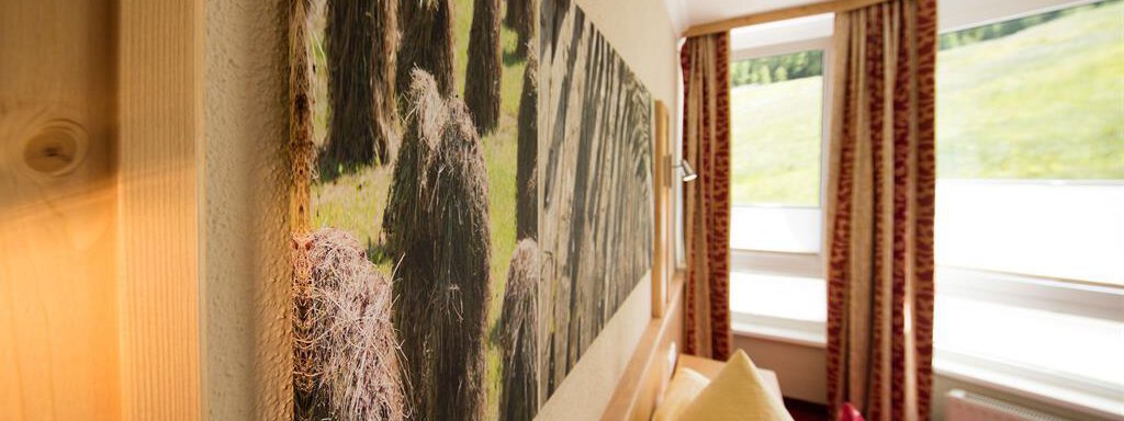A cozy bedroom with bright walls and a large window. On the wall hangs a picture of hay bales in a meadow. - Hotelappart Peter - Sölden