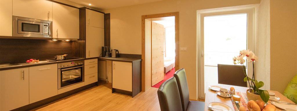 A modern kitchen with elegant furniture and wooden flooring. The dining area is set and offers space for breakfast. - Hotelappart Peter - Sölden