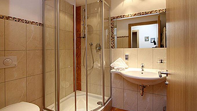 A modern bathroom with a shower cabin, a sink, and a toilet. The walls are tiled in light colors and the floor is tiled as well. - Hotelappart Peter - Sölden