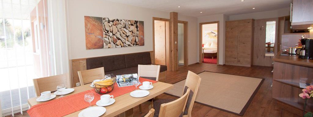 Wohnküche A bright living room with a large table and wooden chairs. There is a cozy atmosphere with decorative elements and a view of the entrance. - Hotelappart Peter - Sölden