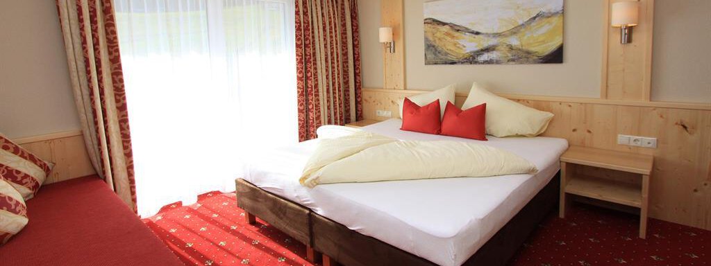 A cozy room with a double bed and red cushions.  
Large windows let in plenty of light and a corner with a red couch. - Hotelappart Peter - Sölden