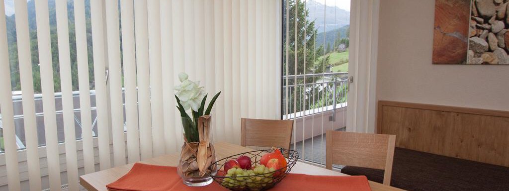 A cozy dining table with fresh fruits and a vase of flowers. In the background, large windows can be seen overlooking nature. - Hotelappart Peter - Sölden