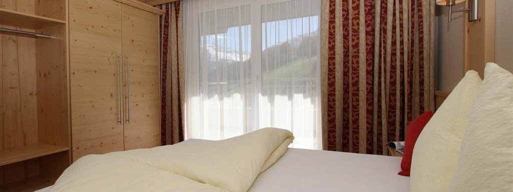 A cozy bedroom with a large window and wood-paneled walls. The beds are simple and inviting, with bright pillows and blankets. - Hotelappart Peter - Sölden