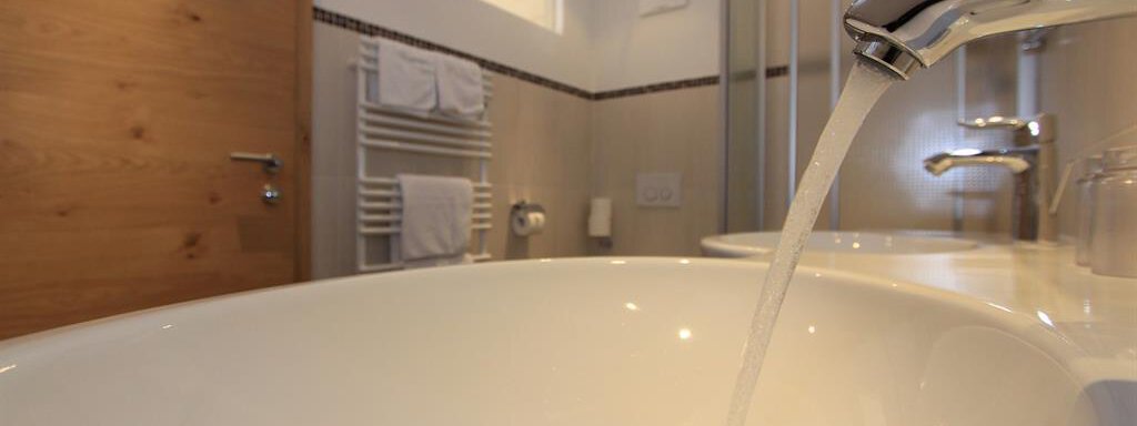 A modern bathroom with a bathtub. Water flows from the faucet and a wooden bench is visible in the background. - Hotelappart Peter - Sölden