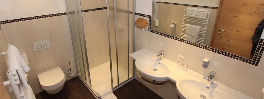 A modern bathroom with two sinks and a shower cubicle. The walls are light and the floor is dark, creating an appealing contrast effect. - Hotelappart Peter - Sölden