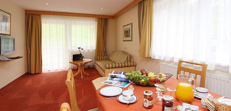 A cozy living area with natural light and a table set with breakfast items. In the background, a sofa and large windows are visible. - Hotelappart Peter - Sölden