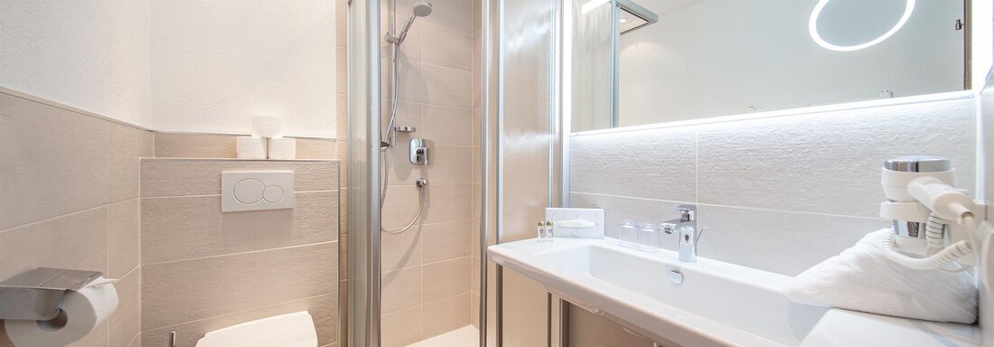 A modern bathroom with a shower, a sink, and a toilet. The walls are light and the room is well-lit. - Hotelappart Peter - Sölden