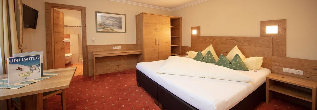 A cozy hotel room with a double bed, a table, and a chair. The room is furnished in warm wood tones and neutral colors. - Hotelappart Peter - Sölden
