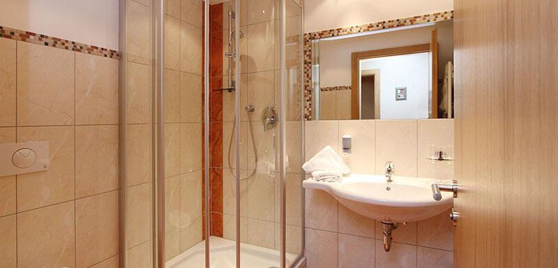 A modern bathroom with a shower cabin and a sink. The walls are tiled in light colors, and the floor has a warm hue. - Hotelappart Peter - Sölden