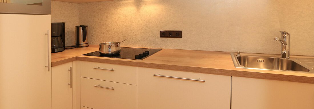 A modern kitchen with white cabinets and wooden countertops. There is a stove, a sink, and kitchen appliances like a coffee machine. - Hotelappart Peter - Sölden
