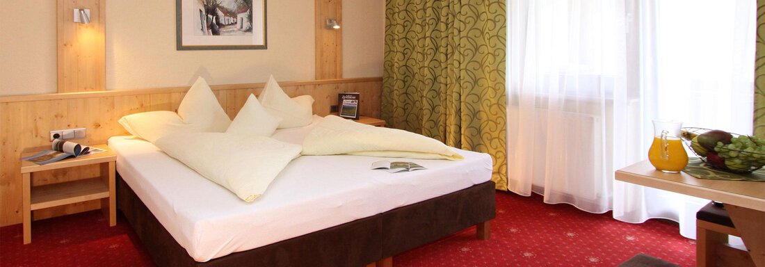 A cozy bedroom with a large bed and bright pillows. Next to the bed is a table with fresh fruit and a drink. - Hotelappart Peter - Sölden