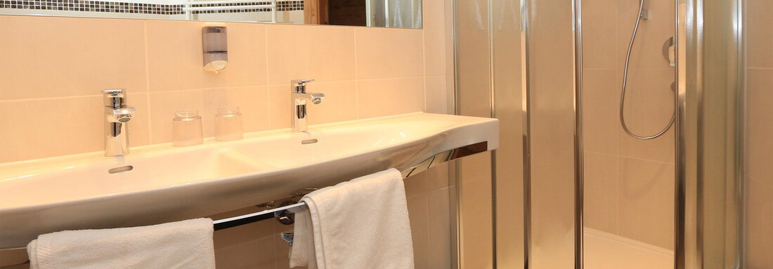 A modern bathroom with a sink and a shower. White towels are ready, and the walls are brightly tiled. - Hotelappart Peter - Sölden