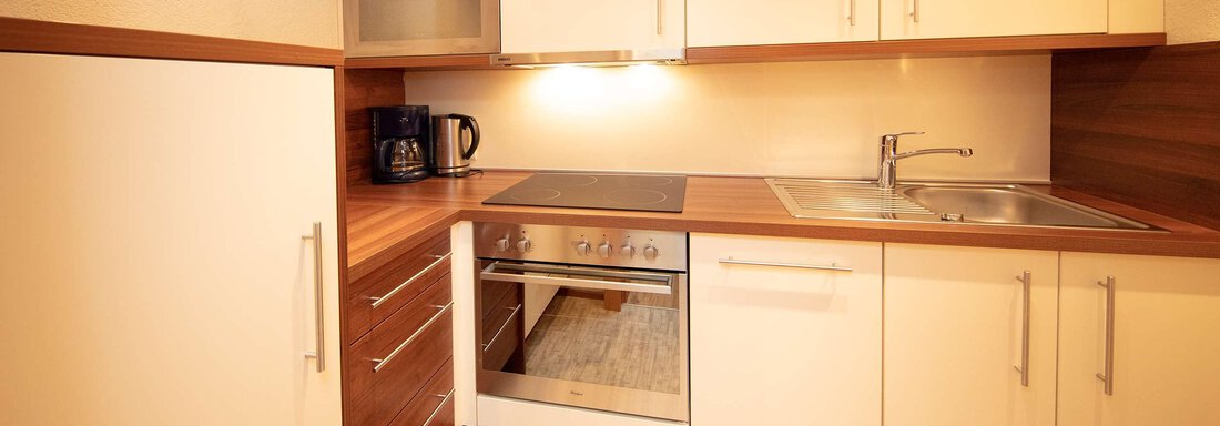 A modern kitchen with bright cabinets and wooden details. It is equipped with a stove, an oven, and a sink. - Hotelappart Peter - Sölden