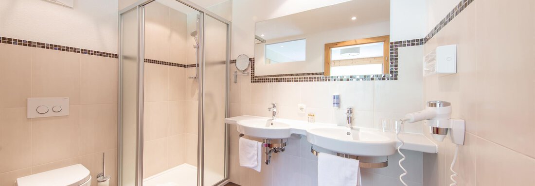 A modern bathroom with a shower and two sinks. It has bright walls and an elegant flooring. - Hotelappart Peter - Sölden