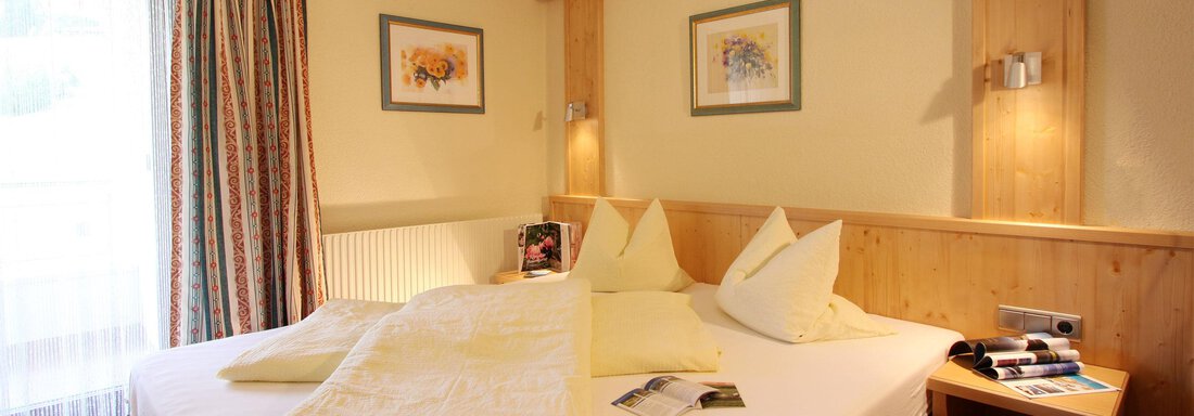 A cozy bedroom with a large bed and numerous pillows. The walls are light, and there are curtains as well as a small bedside lamp. - Hotelappart Peter - Sölden