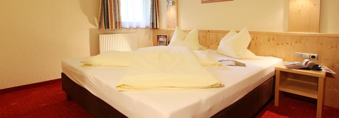 A cozy bedroom with a large double bed and wooden paneling. The walls are painted in warm colors, and there is natural light coming through the window. - Hotelappart Peter - Sölden