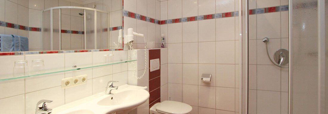A modern bathroom with two sinks and a shower. The walls are tiled, and there are large mirrors. - Hotelappart Peter - Sölden